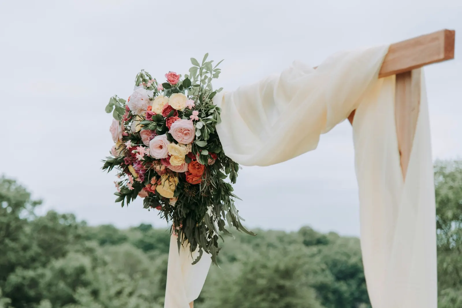 Linen-draped ceremony arch with loose garden roses and greenery