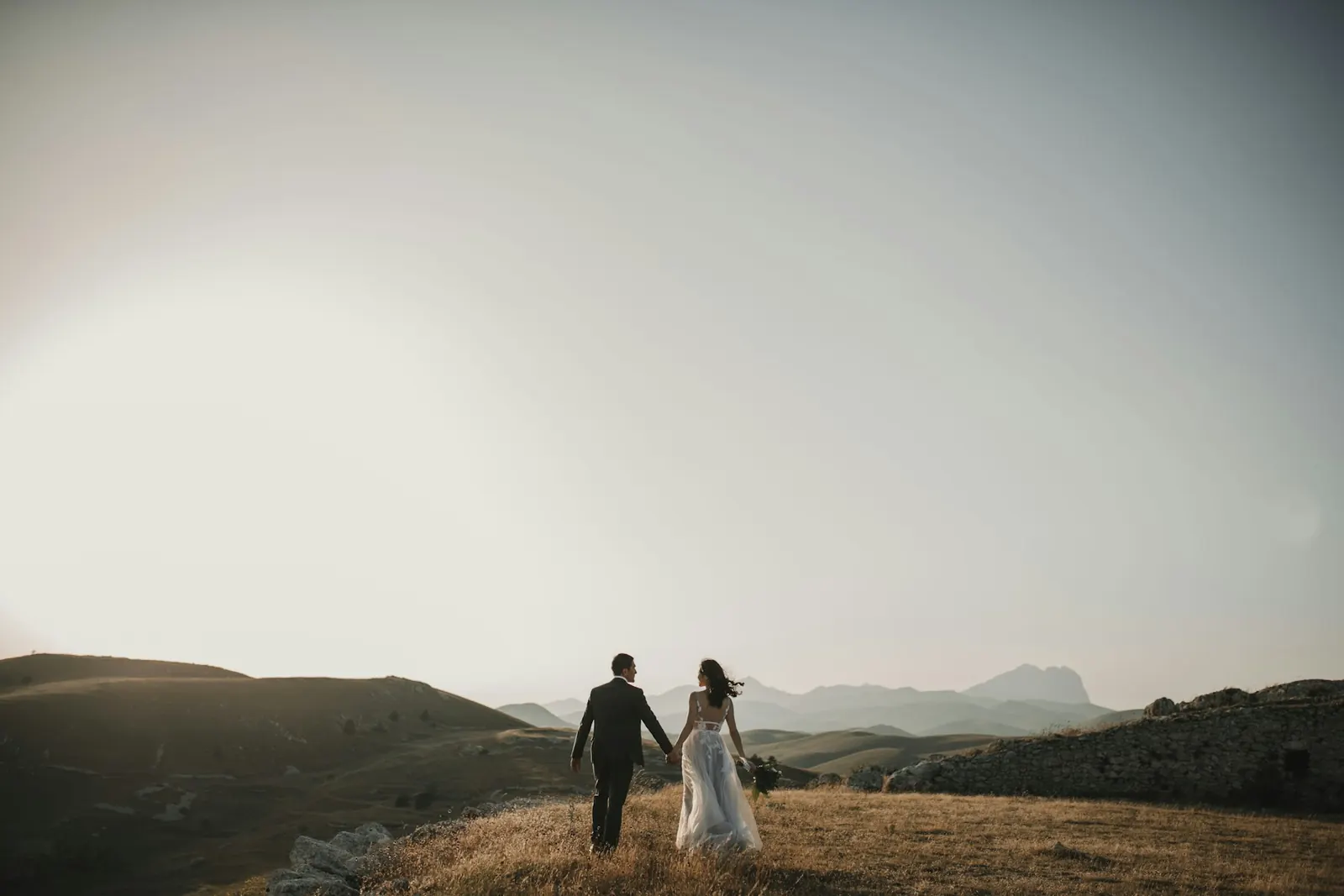 Bride and groom walking hand in hand across an open mountain meadow