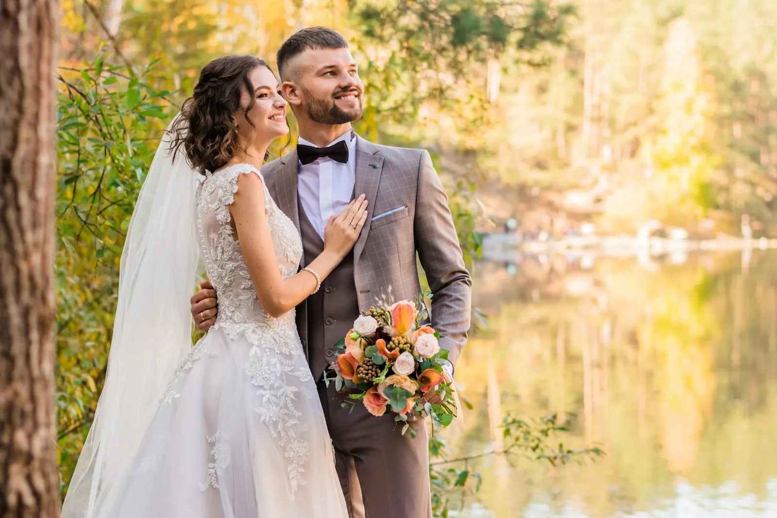 Bride and groom standing by a calm mountain lake with autumn trees